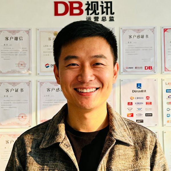 DB视讯运营总监王浩半身照，笑容亲切，身穿休闲商务装，身后背景为公司文化墙上贴满客户感谢信和合作品牌logo